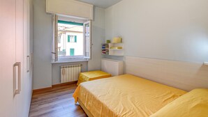 Ein kleines Schlafzimmer mit einem Einzelbett, einem Fenster, einer Heizung und einem Regal mit Büchern.
