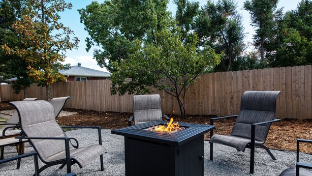 Ein Patio mit einem quadratischen Feuerkorb, umgeben von vier Stühlen und einem Tisch.