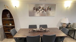 Ein Konferenzraum mit einem Holztisch, sechs grauen Stühlen, einer dekorativen Kiefernzapfen-Mitteldeoration, einem an der Wand hängenden abstrakten Gemälde und einem Bücherregal mit Dekorationsobjekten.