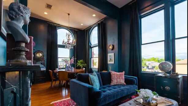 Une pièce avec un canapé bleu foncé, un tapis à motifs rouges, un globe terrestre posé sur une commode et une grande fenêtre donnant sur un beau paysage.