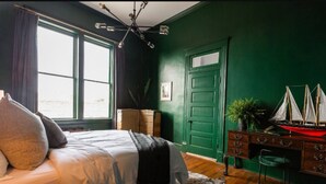 Une chambre à coucher avec un lit, une commode, un bureau, une chaise, une fenêtre et une porte verte.