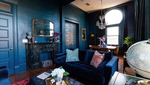 Une pièce avec un mur bleu foncé, une cheminée, un canapé bleu, un globe terrestre et un lustre.