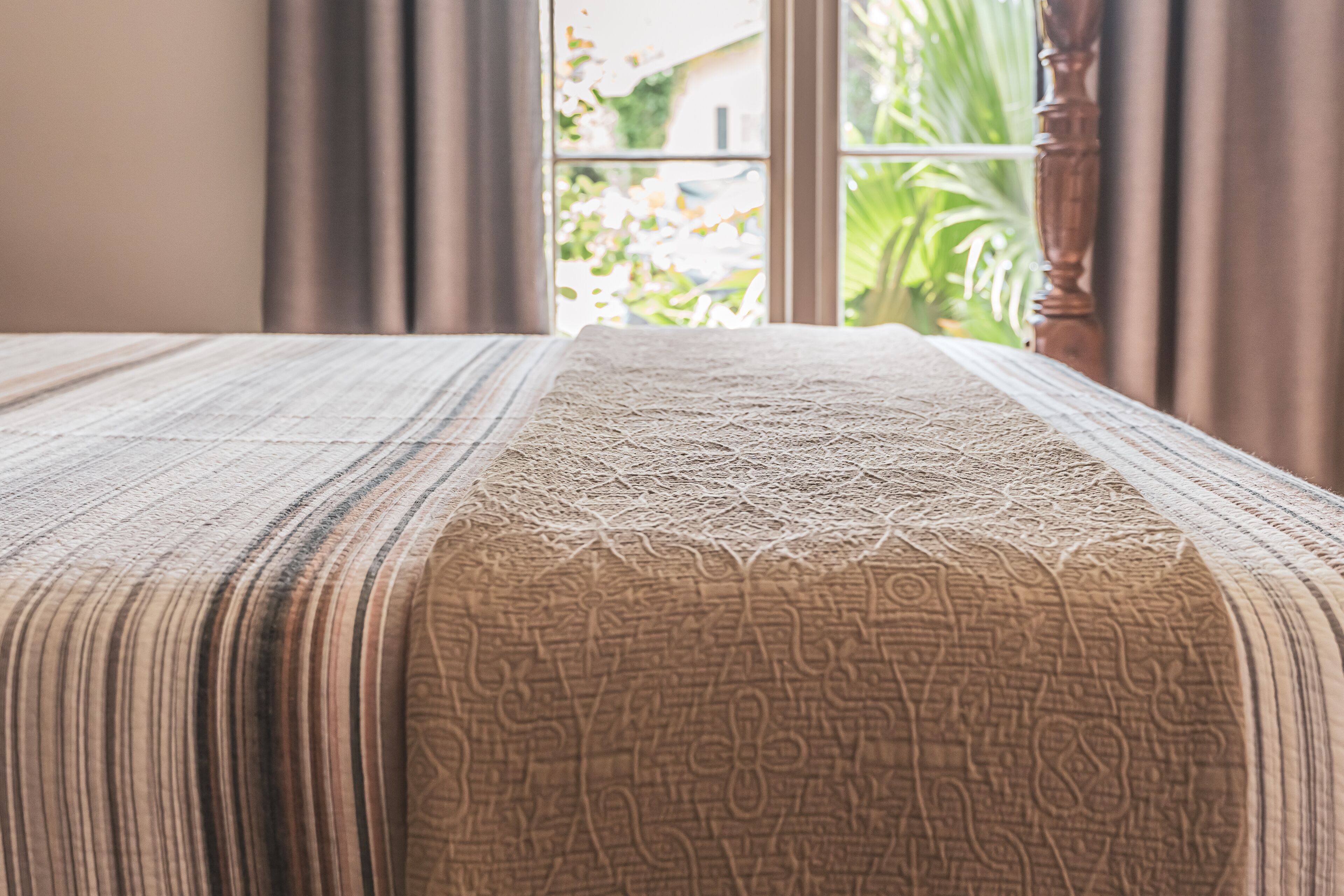 A bed with a patterned bedspread and a view of greenery outside a window.