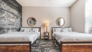 A bedroom with two beds, a black and white patterned rug, a small side table with a lamp, and a wall mural. - Maison Rose - Midcity (Baton Rouge)
