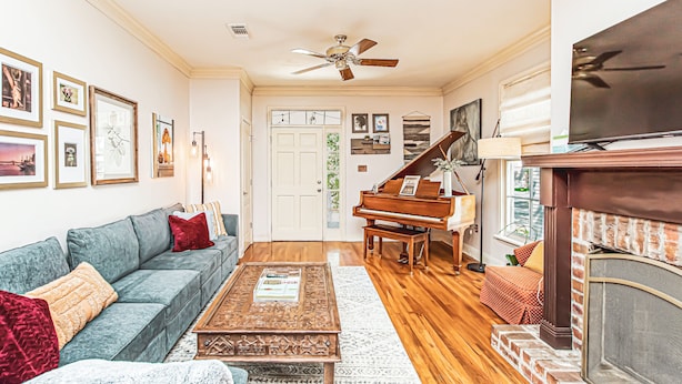 A living room with a sofa, coffee table, fireplace, and a piano. - Maison Rose - Midcity (Baton Rouge)