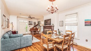 A spacious living room with hardwood flooring, a dining area with wooden chairs, a blue sofa, and a chandelier. - Maison Rose - Midcity (Baton Rouge)