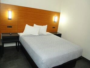 A modern hotel room with a wooden headboard, two bedside tables, a bed with a patterned bedspread, and wall-mounted lights. - Sofi Motel (Los Angeles)