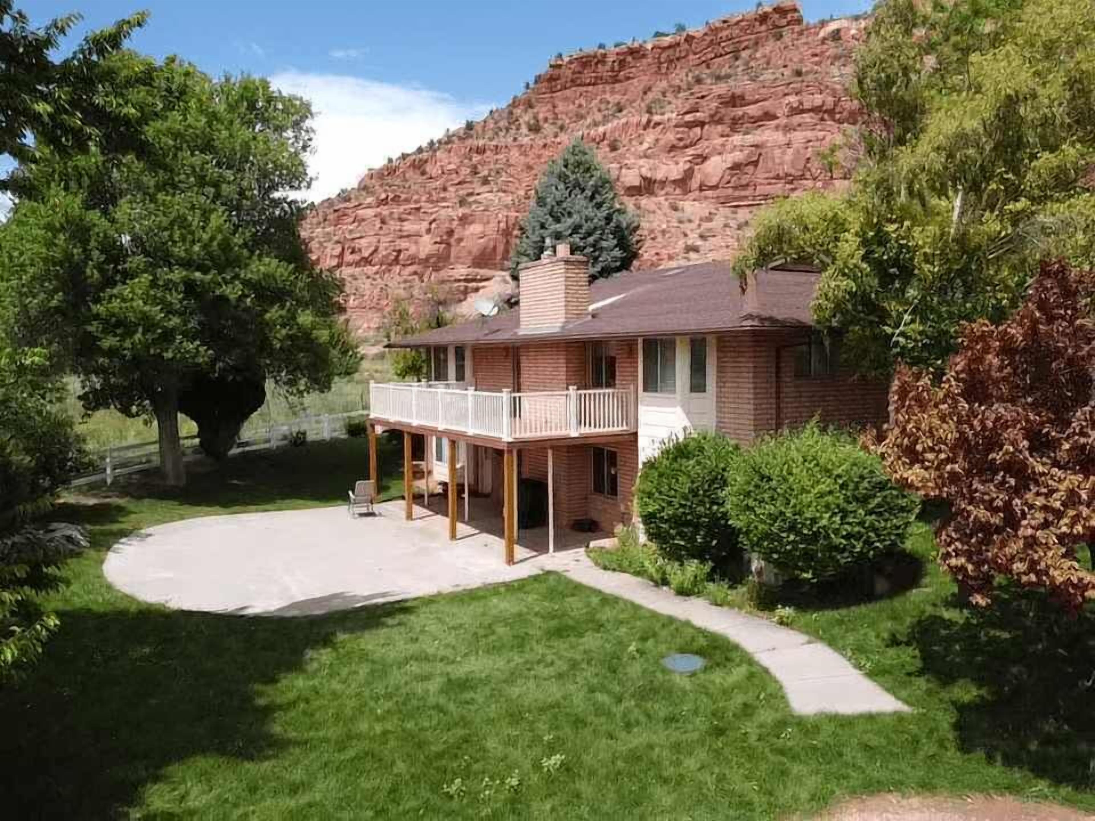 Una casa de dos pisos con balcón, rodeada de un césped cuidado y con montañas al fondo.