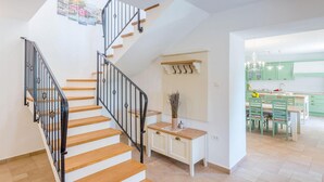 Una cocina moderna con armarios verdes, una zona de comedor con mesa y sillas, y una escalera con escalones de madera y barandillas negras.