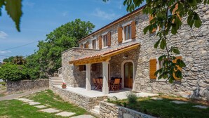 Edificio de piedra con patio cubierto, mobiliario exterior y un muro de piedra que rodea la propiedad.