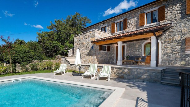 Una villa de piedra con piscina, mobiliario exterior y un patio cubierto.