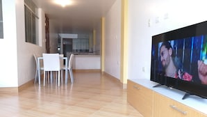 Una sala de estar moderna con televisión, un comedor con sillas y una cocina al fondo.