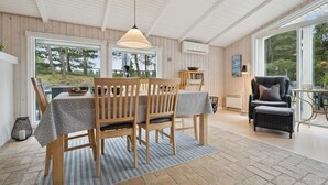Un comedor con una mesa y sillas de madera, una lámpara colgante y vistas al exterior a través de amplios ventanales.