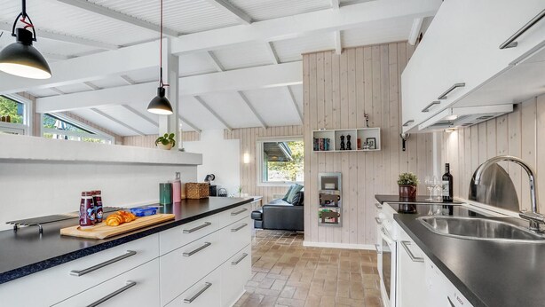 Una cocina moderna con armarios blancos, encimera negra y pileta de acero inoxidable. Hay una ventana que proporciona luz natural y vistas a zonas verdes.