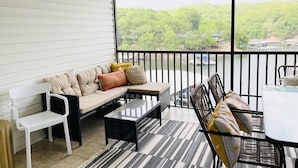 A covered patio with a sofa, chairs, and a table, overlooking a body of water and greenery.