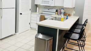 A modern kitchen with white cabinets, a stainless steel trash bin, and a bar area with stools.
