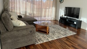 Uma sala de estar com sofá seccional, mesa de centro, televisão de tela plana e ventilador de teto.