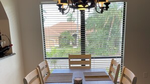 Uma sala de jantar com mesa e cadeiras de madeira, um lustre e uma janela com persianas.