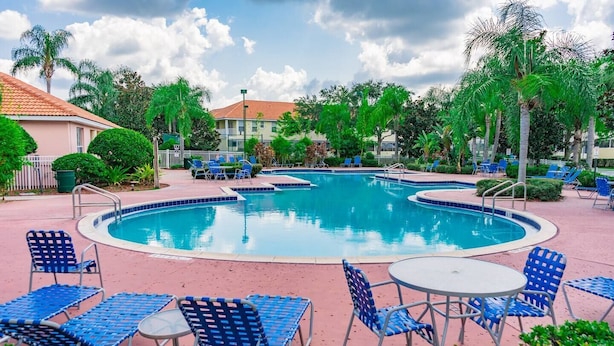 Une piscine entourée de palmiers, avec des chaises et des tables bleues, et un bâtiment doté d’un toit rouge.