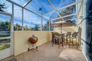A covered patio with a grill, chairs, and an umbrella. - Magical Family Townhome Retreat – Comfort & Convenience Near Top Attractions! (Kissimmee)