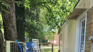 A wooden deck with steps leading to a covered area, a white chair, and a blue folding chair. - Cheerful 3 bedroom Corner Cottage (Jasper)