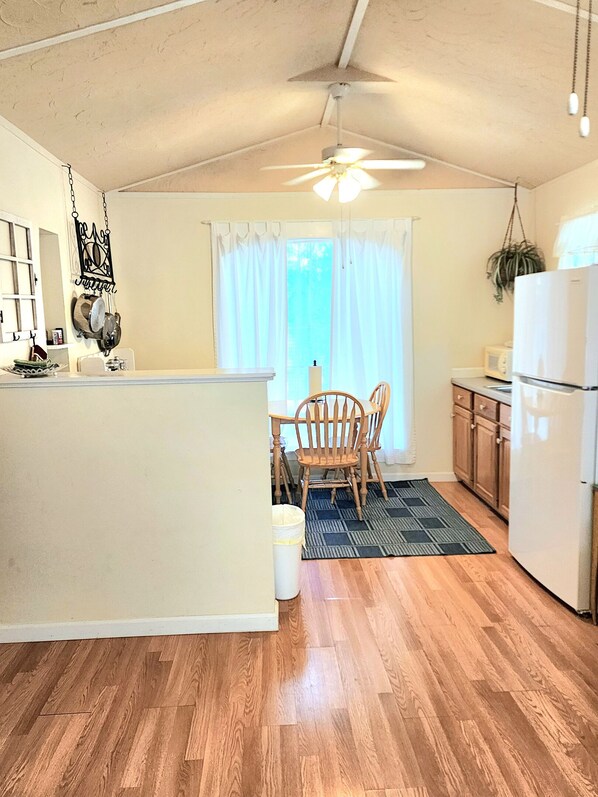 A compact kitchen with a dining area, wooden flooring, and a ceiling fan. - Cheerful 3 bedroom Corner Cottage (Jasper)