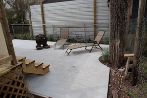 Une terrasse extérieure avec un sol en béton, un foyer et deux chaises longues.
