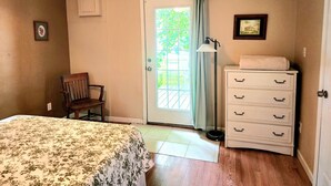 A bedroom with a bed, a chair, a dresser, a lamp, and a door leading to a balcony. - Cheerful 3 bedroom Corner Cottage (Jasper)