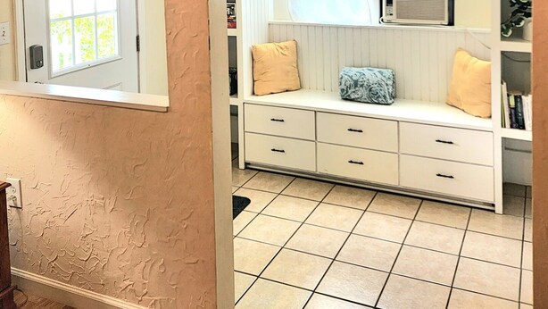A room with a white bench, a window with a curtain, a radiator, and a tiled floor. - Cheerful 3 bedroom Corner Cottage (Jasper)