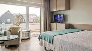 Ein Hotelzimmer mit Bett, Fernseher, Sessel, Tisch und Blick ins Freie.