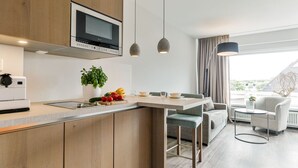 Eine moderne Küche mit integriertem Mikrowellenherd, einer Kaffeemaschine und einem Topf mit Pflanze. Es gibt einen Essbereich mit einer Couch und einem Tisch.