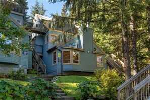 A multi-story house with a staircase leading to the upper levels, surrounded by lush greenery and trees.