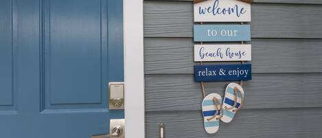 A blue door with a welcome sign and flip-flops hanging on the wall.