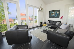 Una sala de estar moderna con sofás de cuero negro, una mesa de centro de vidrio y vistas al mar a través de amplios ventanales.