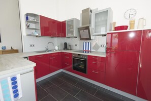 Una cocina compacta con armarios rojos, horno empotrado y microondas.