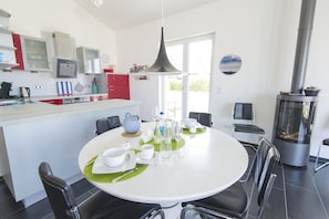 Eine moderne Küche mit Essbereich, mit einem runden Tisch für vier Personen, einem eingebauten Herd und einem großen Fenster, das für natürliches Licht sorgt.