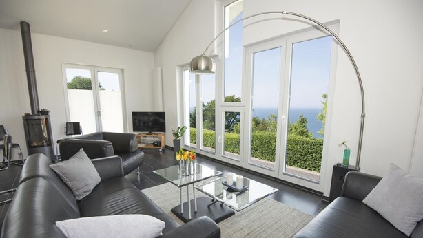Una sala de estar moderna con un sofá de cuero negro, una mesa de centro de vidrio y un ventanal con vista al mar.