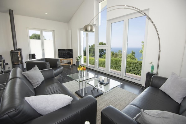 Una sala de estar moderna con un sofá de cuero negro, una mesa de centro de vidrio y un ventanal con vista al mar.