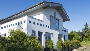 Una casa moderna de dos pisos con fachada blanca, varias ventanas y una puerta azul.