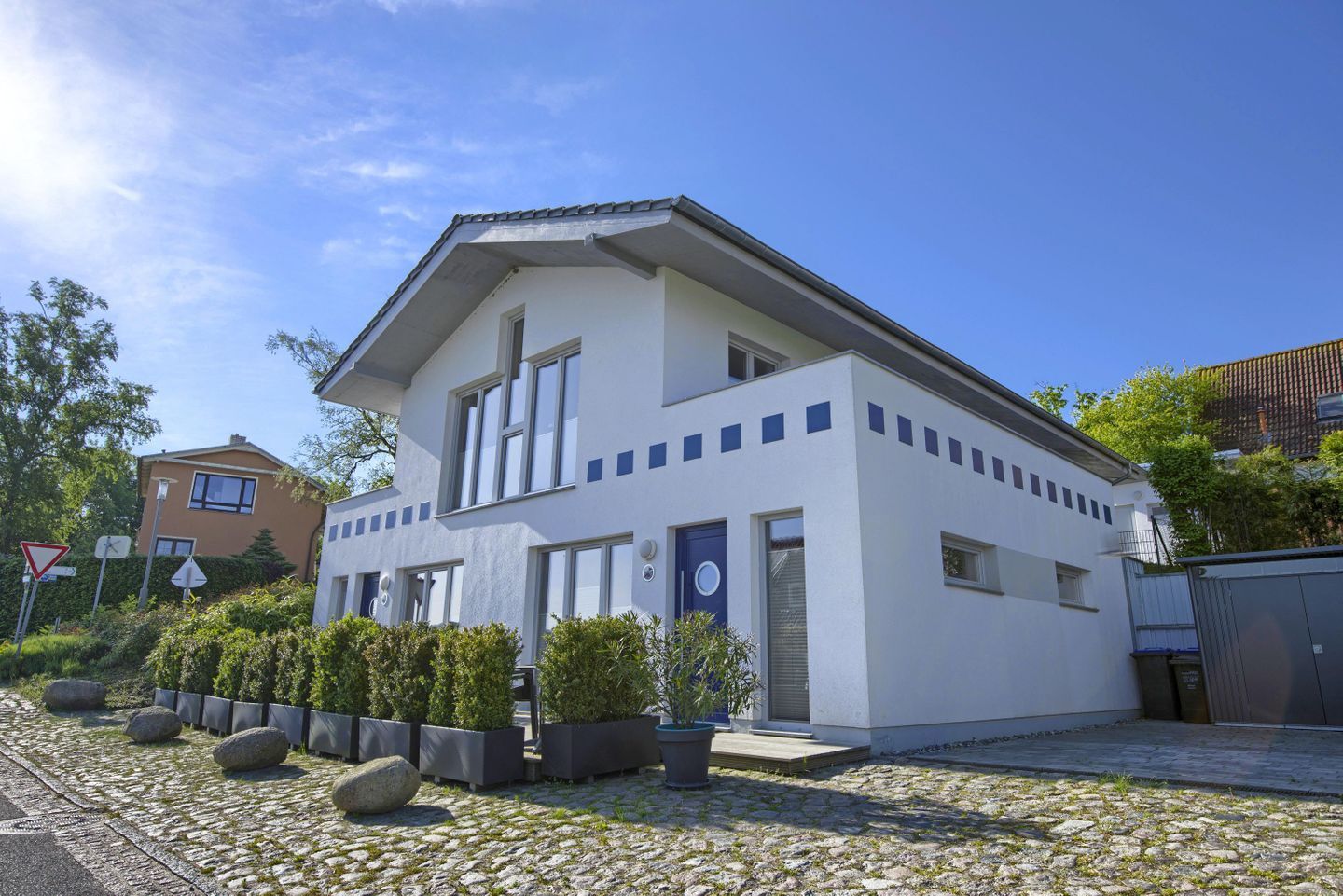 Ein modernes, zweistöckiges Haus mit Flachdach, großen Fenstern und einem gepflasterten Auffahrt.