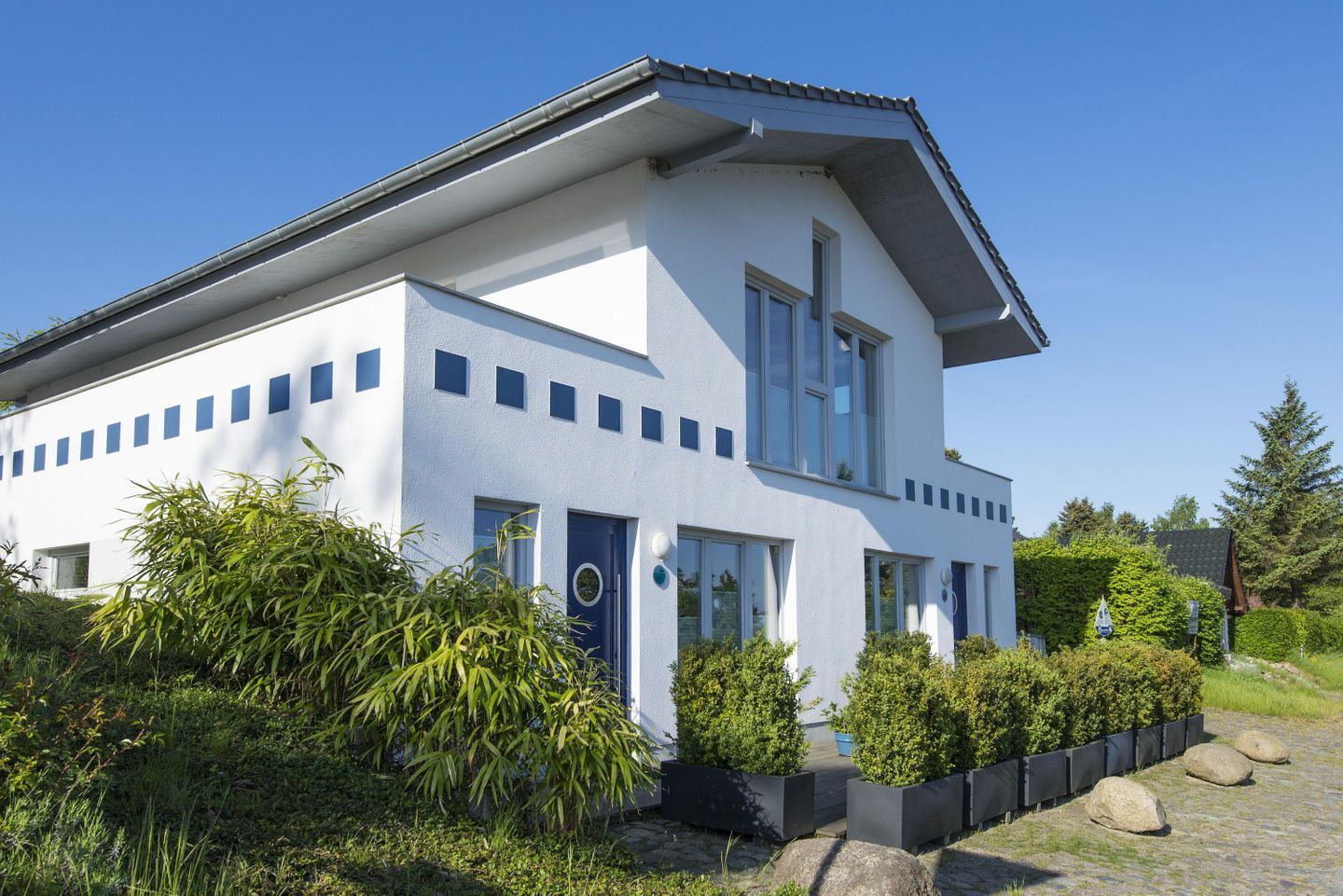 A modern two-story house with a white facade, multiple windows, and a blue door.