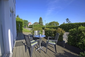 An outdoor deck with a table and two chairs, surrounded by greenery and a clear sky. - Beautiful 2-room vacation apartment with a terrace - Haus Ostseeblick 1 FeWo Backbord - (Lohme)