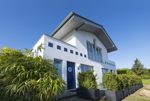A modern two-story house with a flat roof, large windows, and a blue door. - Beautiful 2-room vacation apartment with terrace - Haus Ostseeblick 1 FeWo Steuerbord - (Lohme)