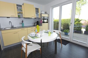 A modern kitchen with yellow cabinets, a white dining table, and a view of the garden through large sliding doors. - Beautiful 2-room vacation apartment with a terrace - Haus Ostseeblick 1 FeWo Steuerbord - (Lohme)