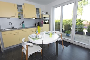 Une cuisine moderne avec des meubles de couleur jaune, une table à manger blanche et une vue sur le jardin grâce à de grandes portes coulissantes.