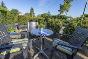 An outdoor patio with a round table and four chairs, surrounded by greenery and a clear sky.