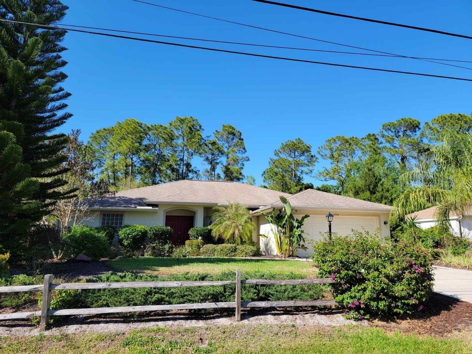 A single-story house with a front porch, surrounded by a wooden fence and various plants.