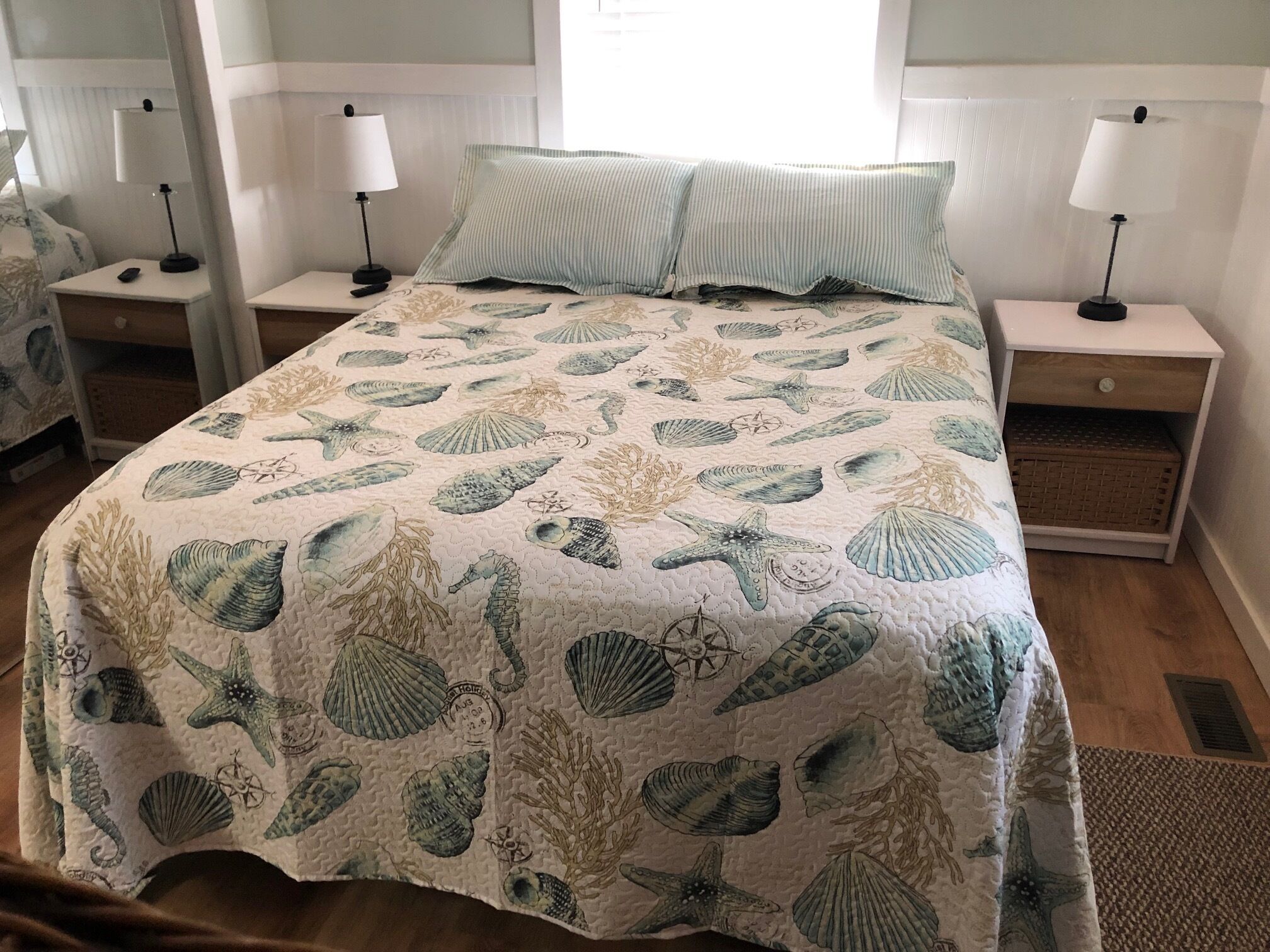 A bed with a nautical-themed quilt, two bedside tables with lamps, and a nightstand with a basket.