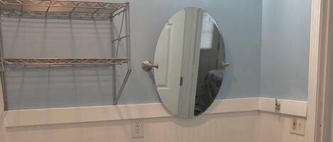 A bathroom with a white toilet, a green vanity with a black countertop, a round mirror, and a wall-mounted light fixture.