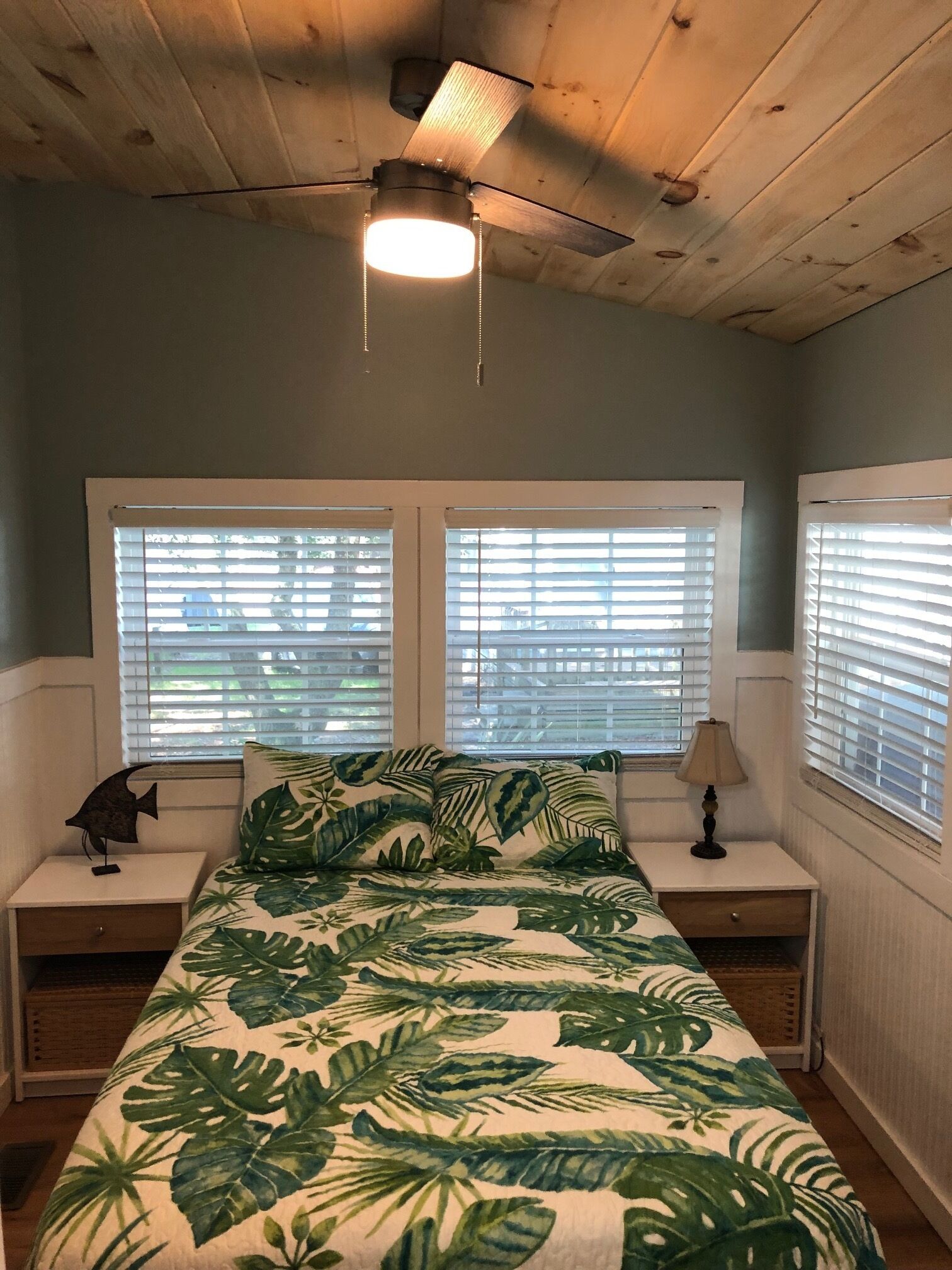 A bedroom with a bed, two nightstands, a ceiling fan, and windows with blinds.